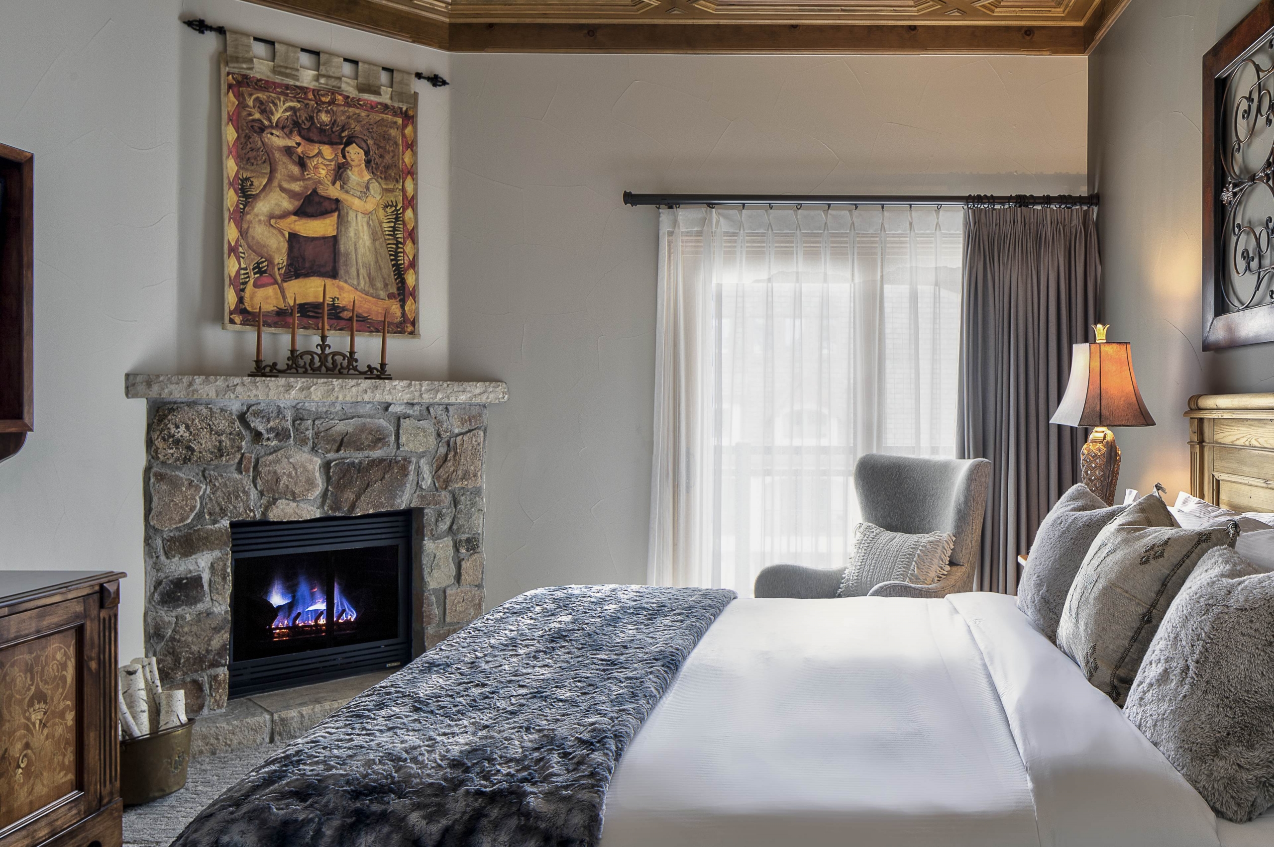 Upscale bedroom featuring a stone fireplace, elegant artwork, and a plush bed with a view of a snowy terrace.