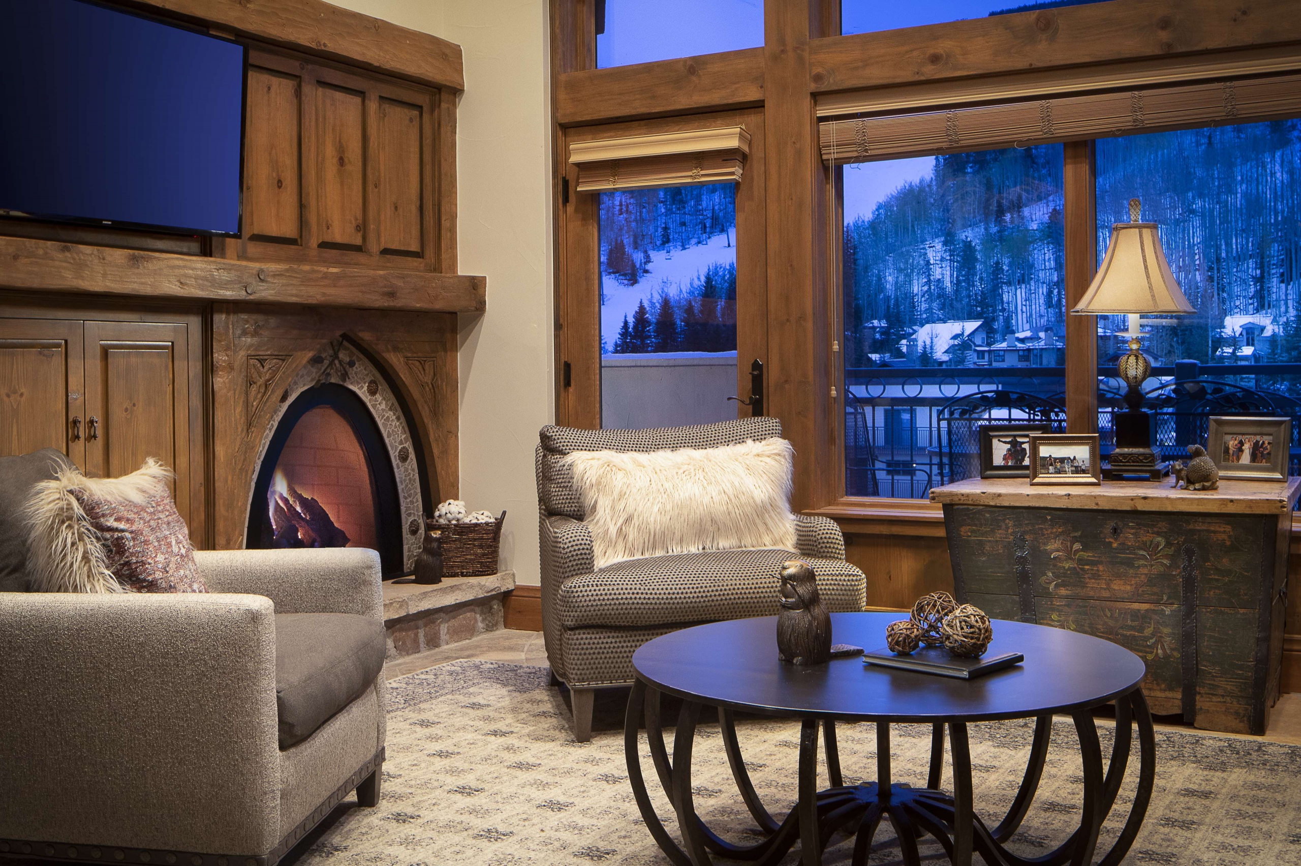 A warm residential seating area with a unique arched fireplace, plush armchairs, and a view of snowy Vail ski slopes.