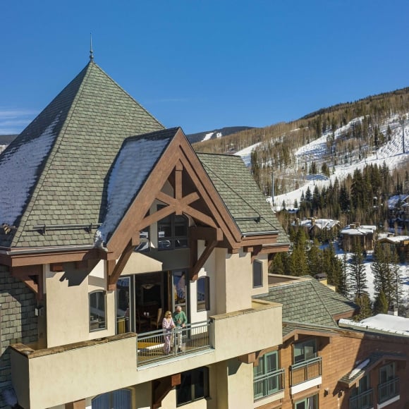 Exterior view of The Hythe Vail showing a luxury suite balcony with guests, set against a snow-covered mountain backdrop.