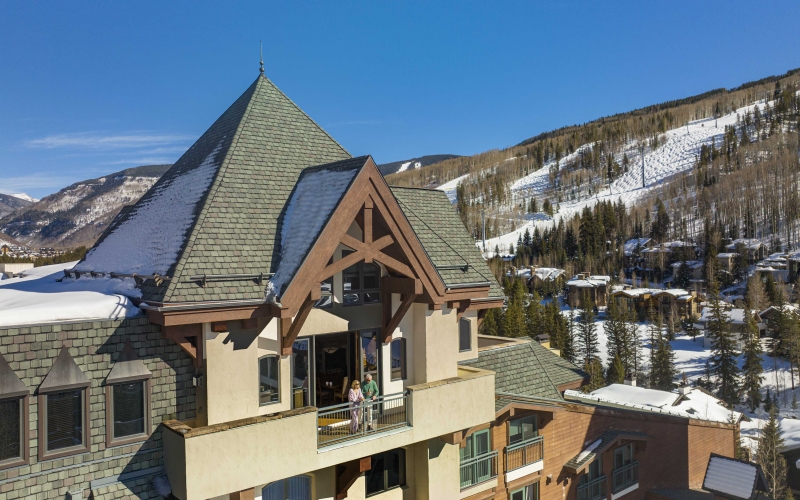 Exterior view of The Hythe Vail showing a luxury suite balcony with guests, set against a snow-covered mountain backdrop.