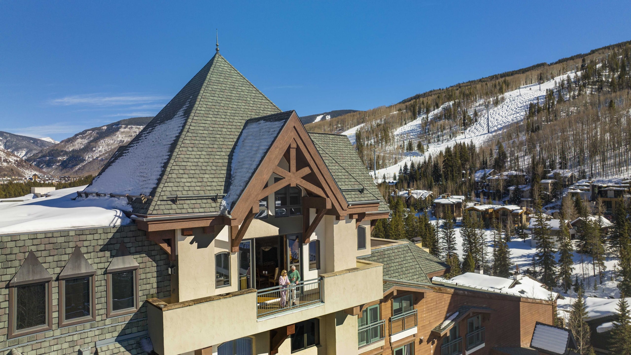 Exterior view of The Hythe Vail showing a luxury suite balcony with guests, set against a snow-covered mountain backdrop.